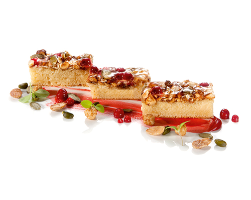 Baton biszkoptowy Powerschnitte w jasnym kolorze, pokryty mieszanką musli z pestkami dyni, orzechami laskowymi, migdałami, płatkami owsianymi i żurawiną, 3 x 7 cm.
