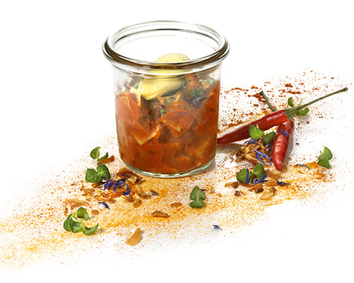 Vegan curry sausage in roasted onion-mayonnaise sauce vegan sausage substitute based on pea protein in a curry sauce, with roasted onions and a mayonnaise-curry garnish, in a tall preserving jar.