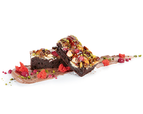 Powerschnitte dunkel dunkler Biskuitriegel, bedeckt mit einem Müslimix aus Pistazien, Haselnüssen, Walnüssen, Mandeln,  Haferflocken und Preiselbeeren, 3 x 7 cm.