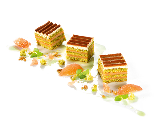 Grapefruit-Matcha-Würfel saftiger Matcha-Biskuit, geschichtet mit fruchtiger Grapefruitcreme, zartschmelzender  Buttercreme und Schokolade, 4 x 4 cm.